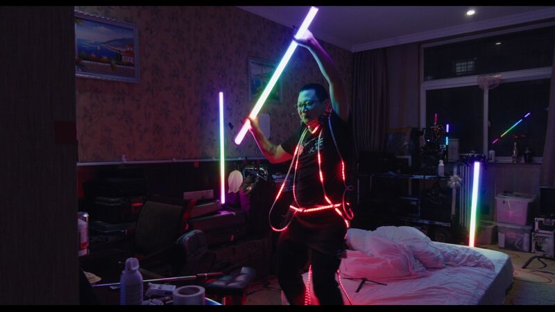 A man in a dark bedroom dances holding a glow stick.