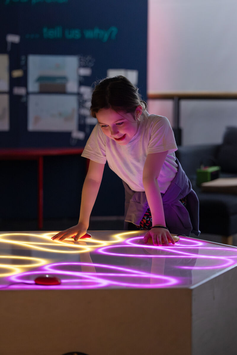Child playing with Soundplay equipment in DCA Create Space an dpressing buttons to control yellow and purple lights