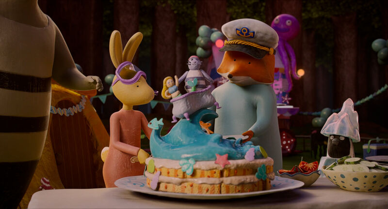 An animated rabbit and fox stand next to a cake which has an under the sea theme.