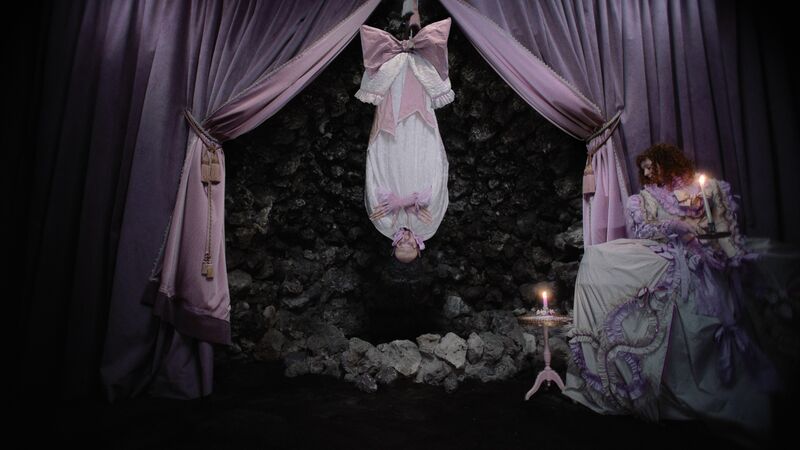 Figure hanging upside down above a curtained area