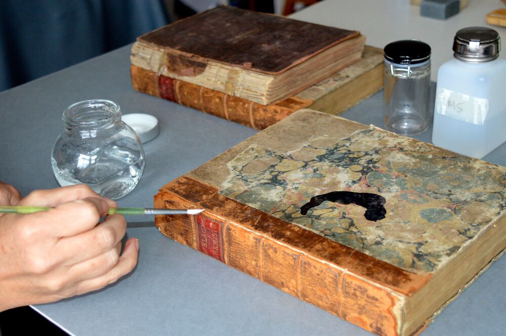 Person painting a solution onto an old book