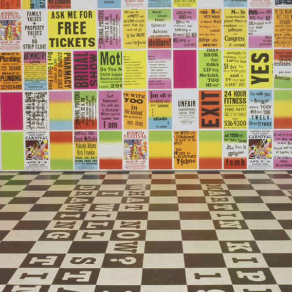 A selection of images from Allen Ruppersberg's exhibition at DCA. The floors are black-and-white check, and there are bright, multicoloured graphic posters all over the walls with different slogan and sentences on them.