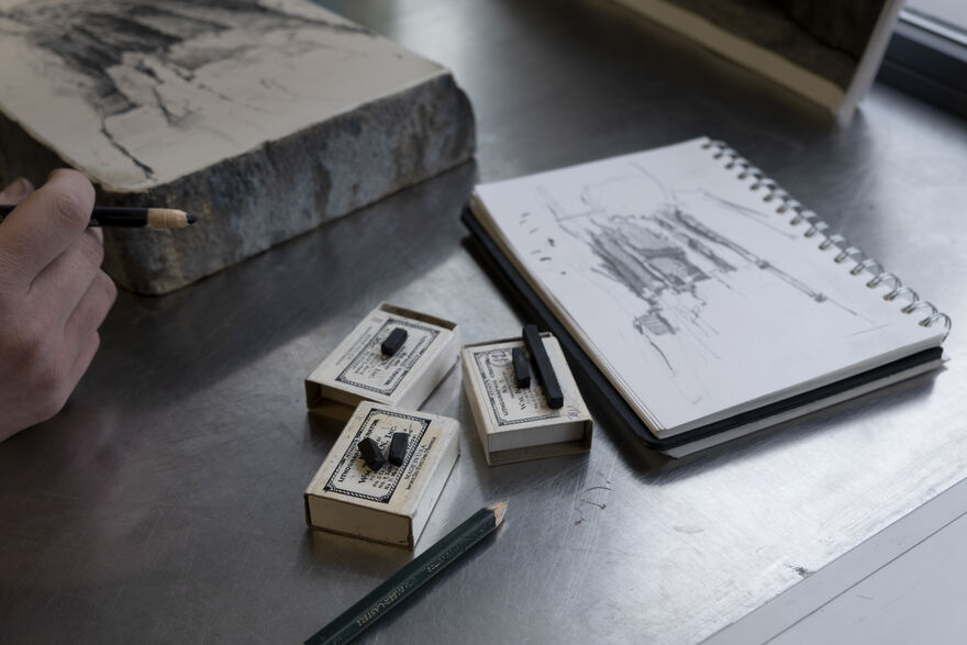 Sketchbook and drawing tools beside a stone 