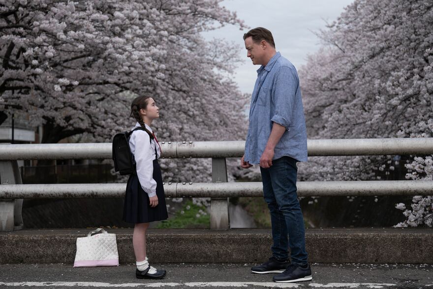 A man and a little girl stand on a bridge looking at one another, while cherry blossom blooms in the background