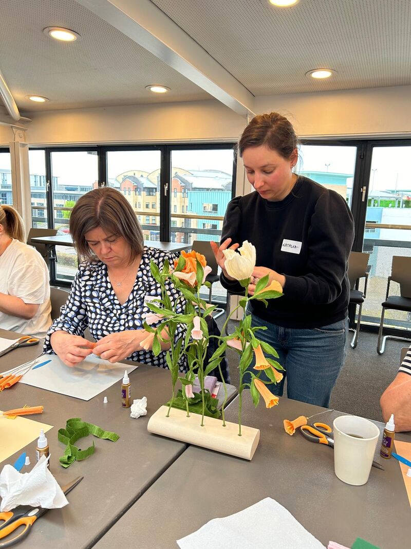 Tutor showing paper flower making techniques to a group of people