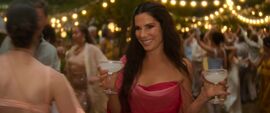 A woman walks through a garden party holding two margaritas