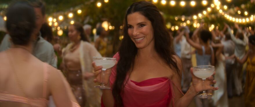 A woman walks through a garden party holding two margaritas