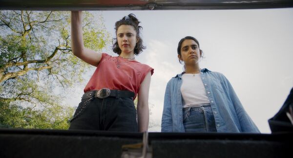 Two women look under the roof of a car.
