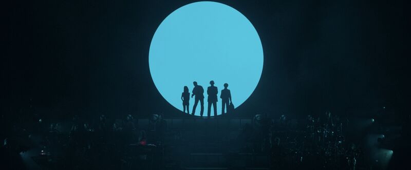 Pulp standing in front of a giant blue round light