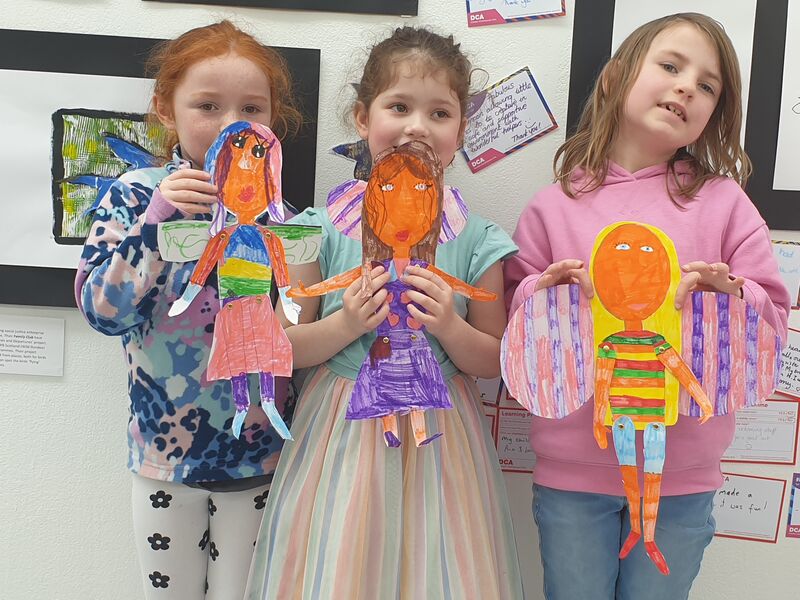 Three children holding up paper dolls