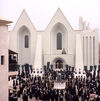 Set of a curch surrounded by a crowd holding crosses and black flags