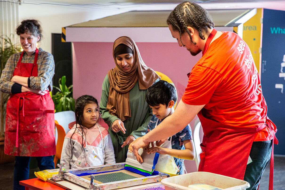 Learning tutor showing a mother and two children how to screen print