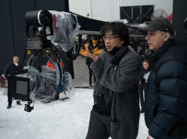 Director Bong Joon Ho stands on a snowy set near a camera, directing his crew