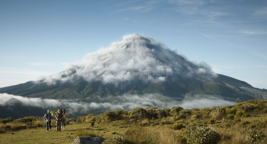 A huge mountain with three children hiking towards it.