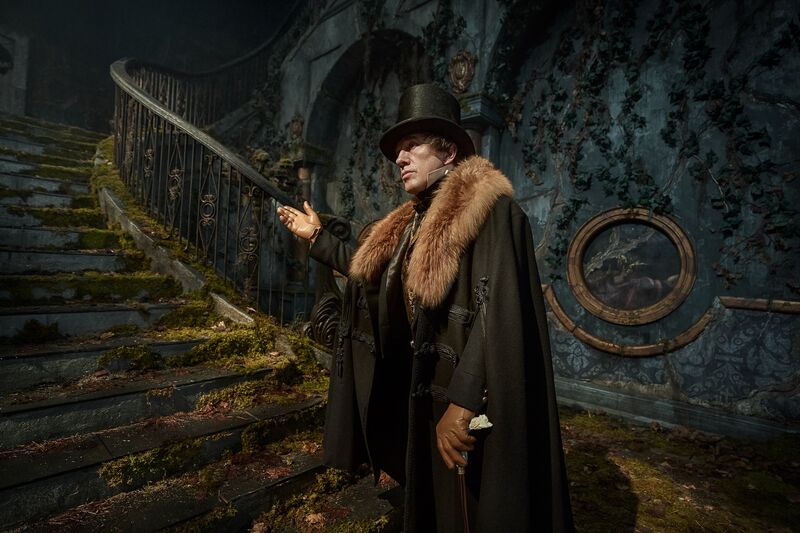 A man in a top hat gestures to some creepy stairs.