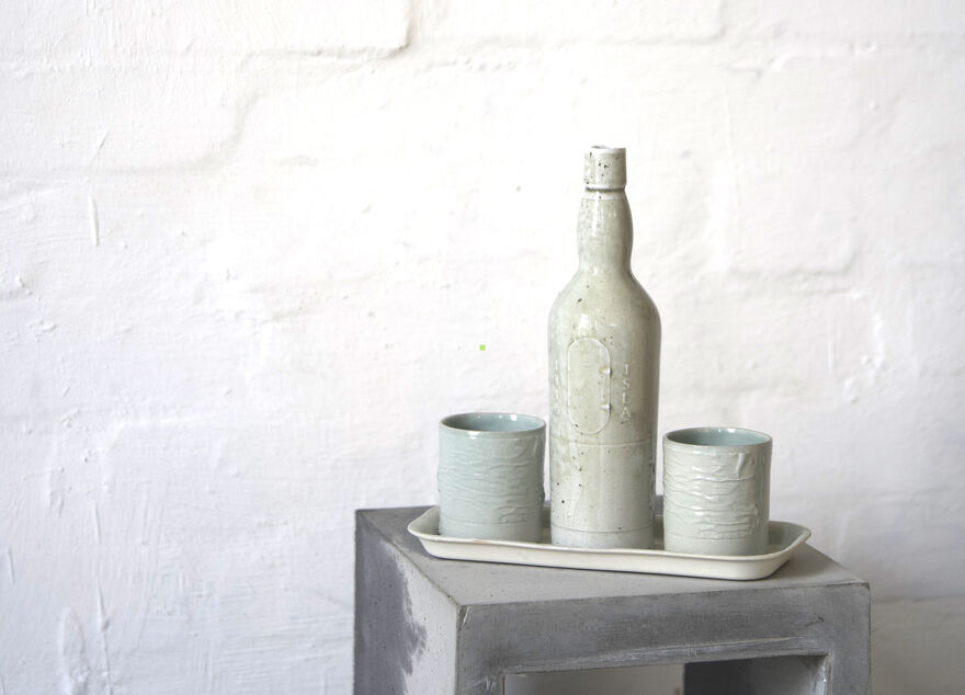 Ceramic bottle on a tray beside two textured ceramic cups