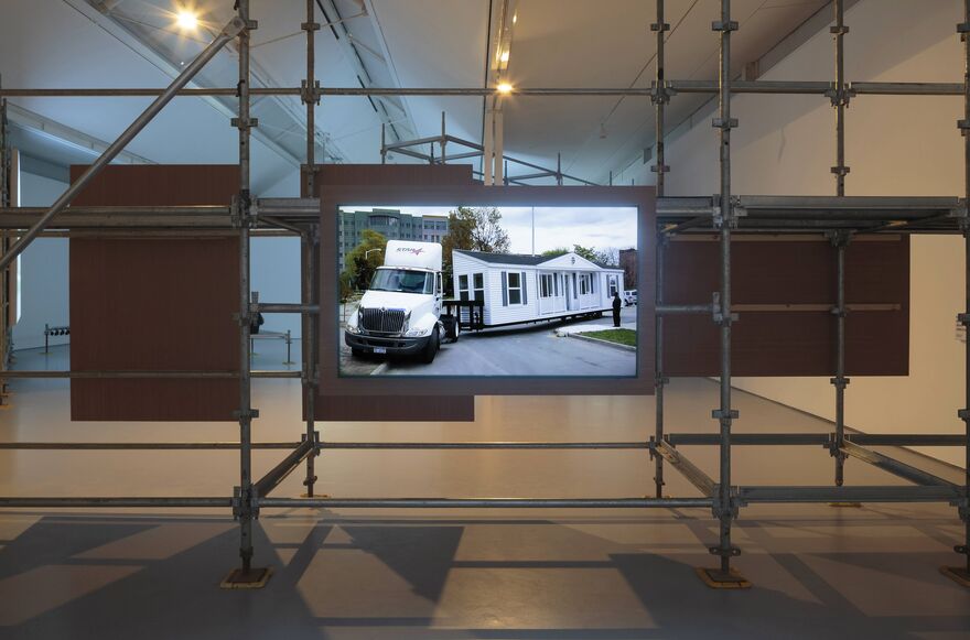 A television suspended on scaffolding shows a van pulling a mobile home. From Mike Kelley's Mobile Homestead.