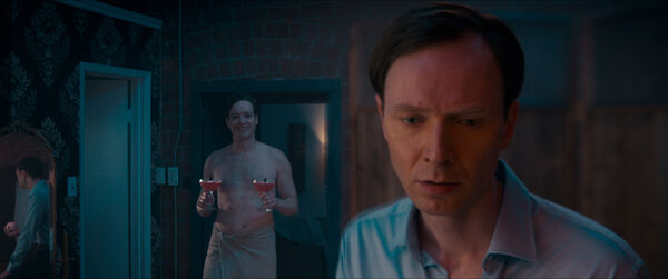 Close up of peosons face with a man in the background holding two cocktails