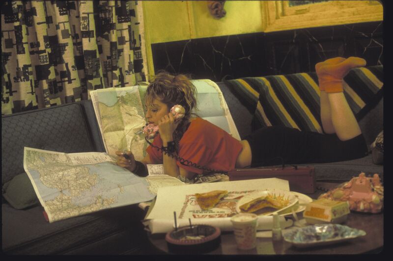 A woman sits on a sofa, looking at maps and talking on a pink telephone