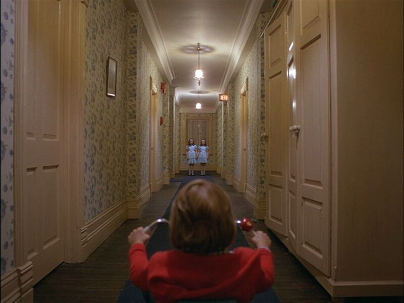 Child on a trike in a hotel corridor with two girls standing at the end