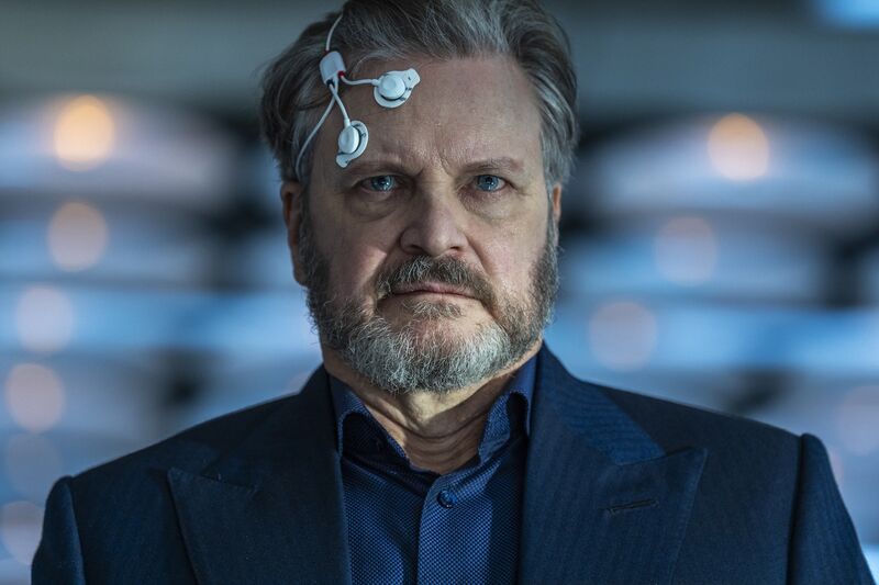 A close view of a man with electrodes stuck to his head, he has a pained expression. Colin firth is the man.