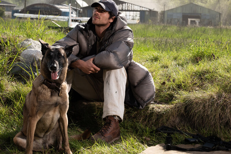 A young man and his dog sit in a field