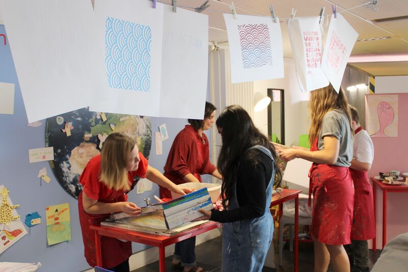A group of five people in red aprons are screen printing in DCA's Create Space