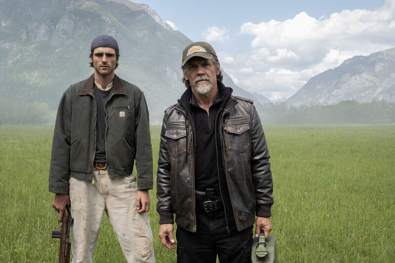 Two men carrying weapons stand in a deserted rural landscape