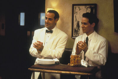 Two men wearing white suits and looking like waiters, clap.