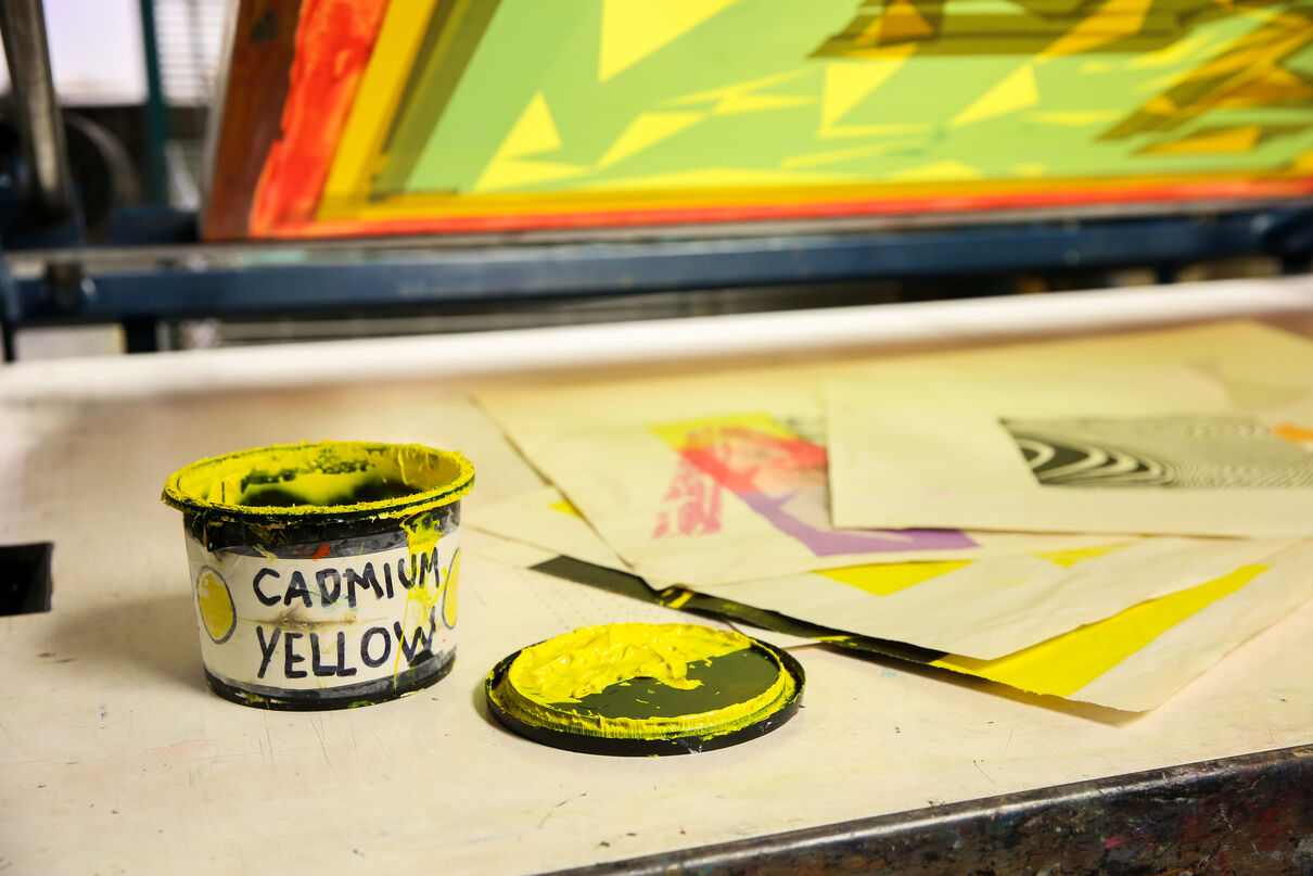 Yellow ink and prints laid out on a screen printing table