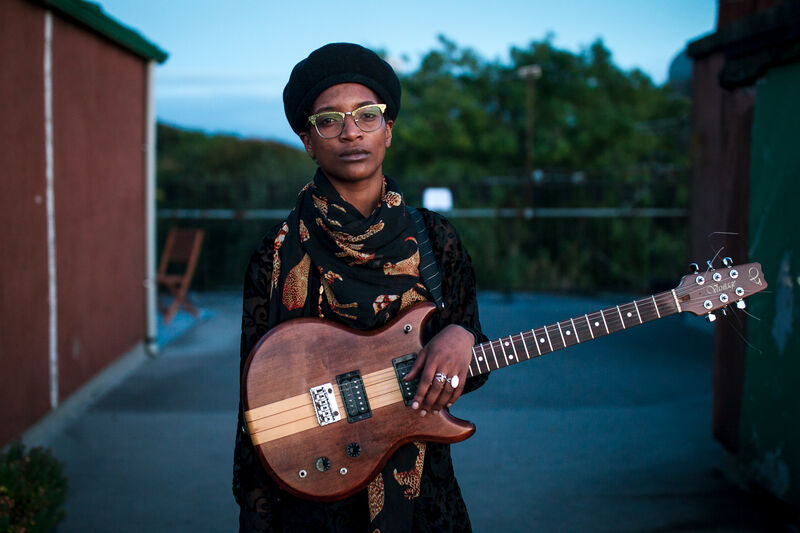 A woman looks into the camera while holding a guitar