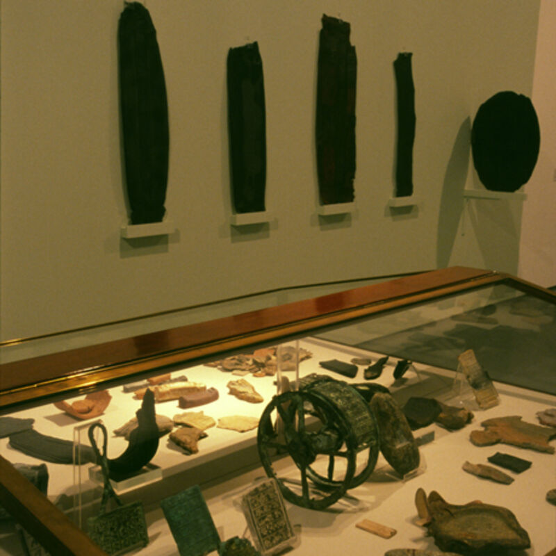 rom Will Maclean's exhibition in DCA. A glass case is filled with small objects, including stones, a wheel and relics.