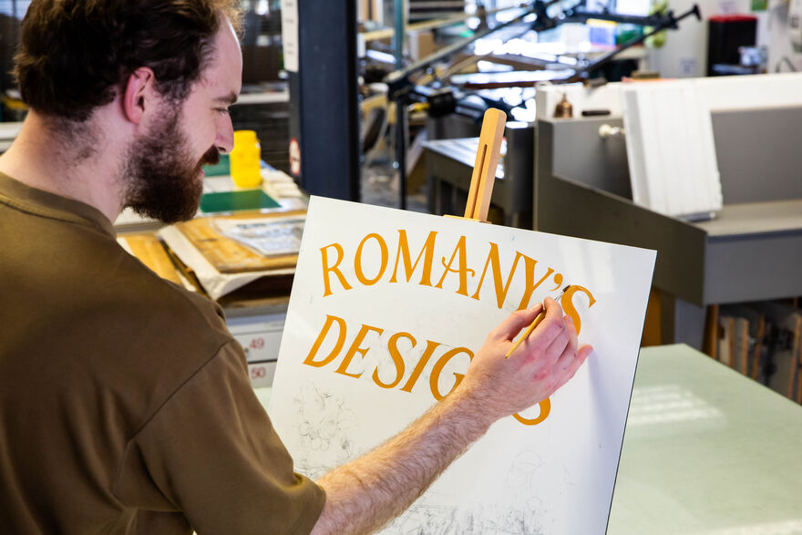 Person painting letters on a sign with yellow lettering