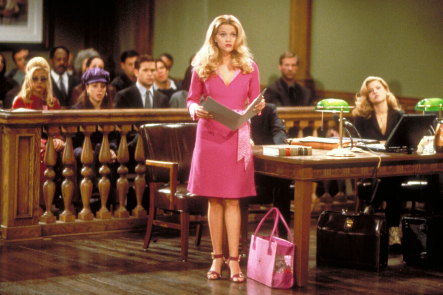 A girl in a bright pink dress stands in a court room.