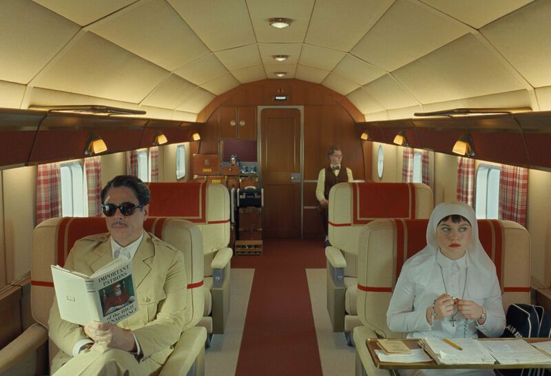 A man in a cream suit and sunglasses sits on a private plane next to a nun dressed all in white