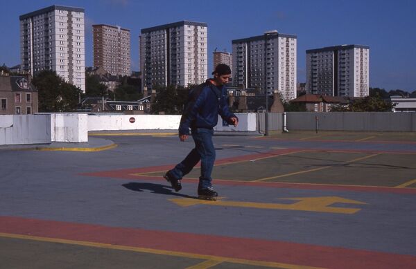 From Roderick Buchanan's exhibition, a film still of a person rollerblading in Dundee behind the multi-story flats.