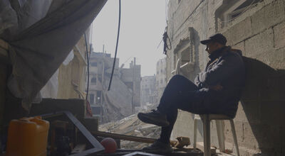 A man sits on a chair outside in Gaza, surrounded by ruins from bombing.