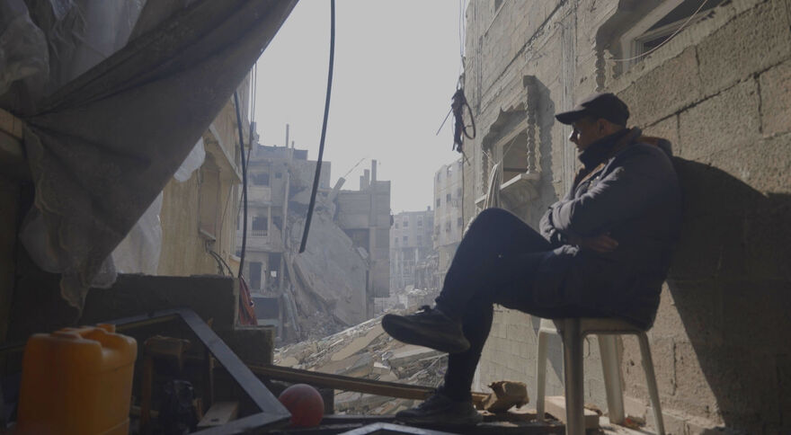 A man sits on a chair outside in Gaza, surrounded by ruins from bombing.