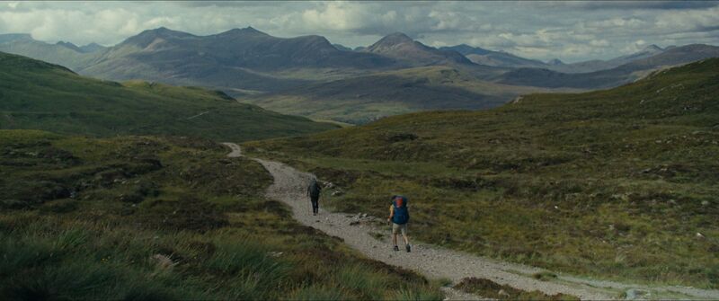Two men in hiking gear walk up a path towards Scottish mountains