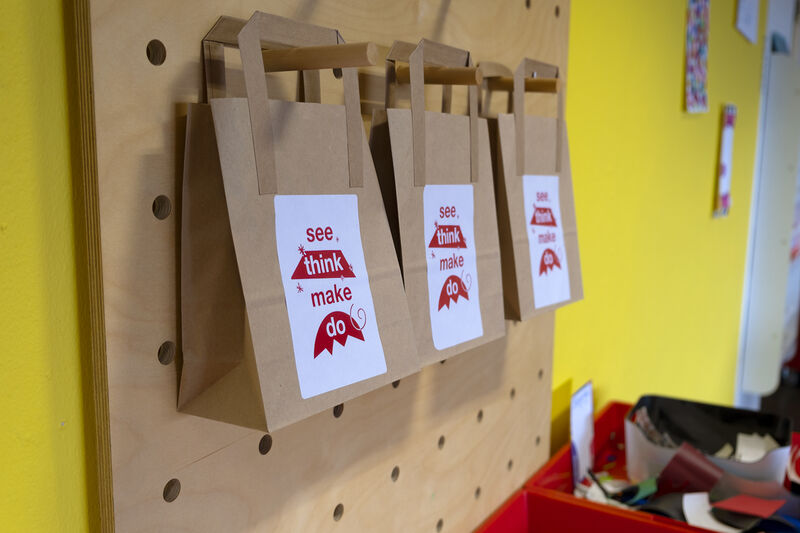 Three paper bags hanging on a peg board with 'see, think, make, do'stickers