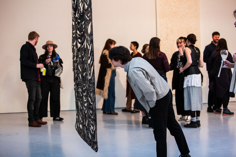 Person looking at a hanging artwork in DCA galleries as groups of people talk in the background