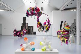 A gallery space with sculptures with casts large suspended scupltures and visible in the background photos on the wall