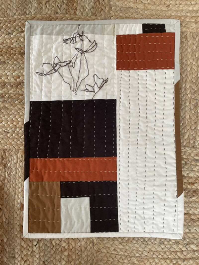 Quilted wall hanging made with black, orange, cream and brown fabric with embroidered flowers