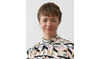 A white women with short brown hair smiles at the camera. She is wearing a geometric patterned top. 
