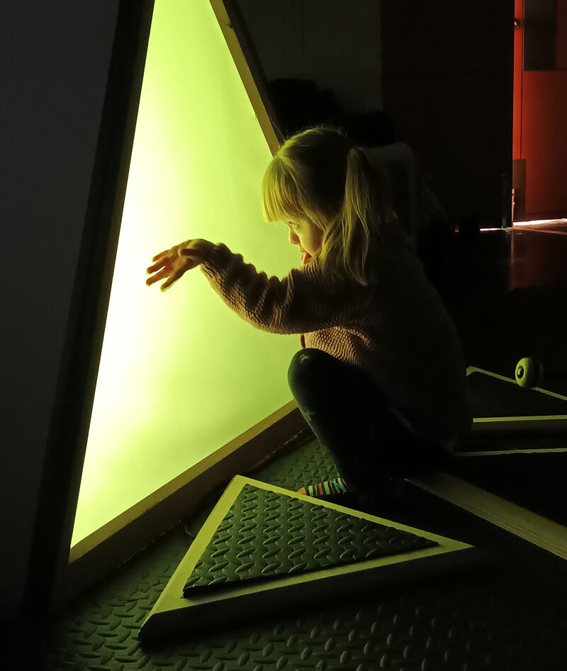 Child looking into a triangular box that's lit up with a yellow light