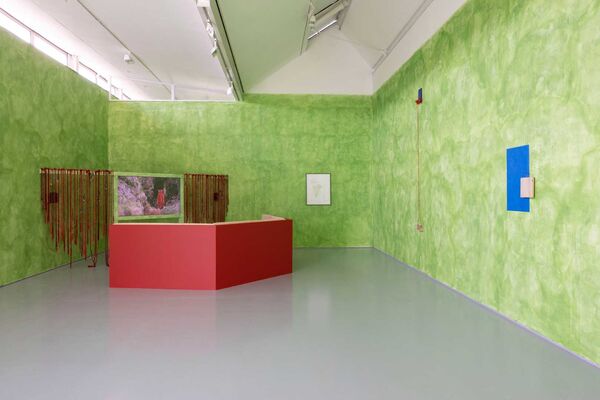 An installation view of the exhibition, showing the film on a screen in front of the red seating area. The gallery walls are mottled green.