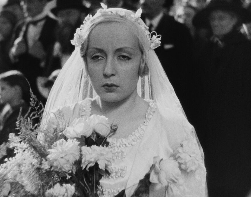 A black and white film still of a serious-looking bride in a 1930s wedding dress
