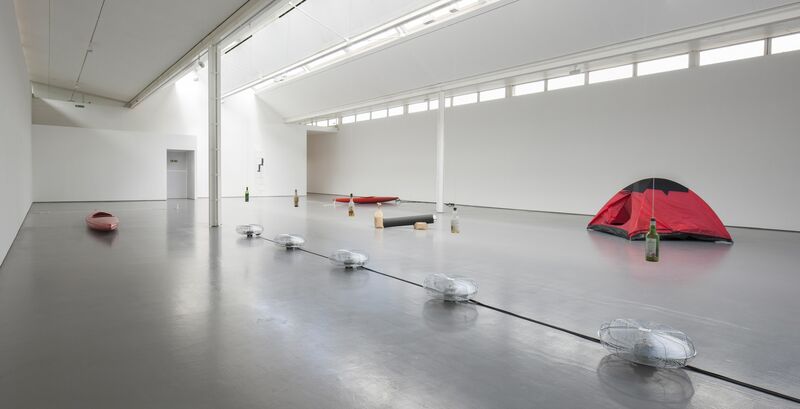DCA Galleries during Roman Signer's exhibition. Electric fan, which are facing skyward, blow beneath glass bottles tied by string from the ceiling. A red tent and a red kayak can be seen in the background.