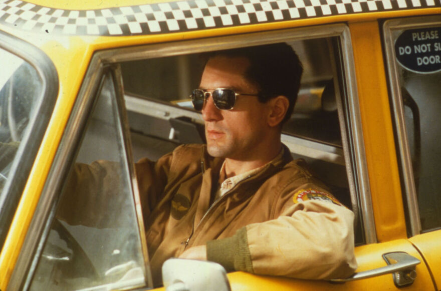 Robert De Niro driving a yellow taxi, wearing shades.