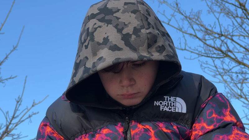 A teen boy in a winter coat looks sad 